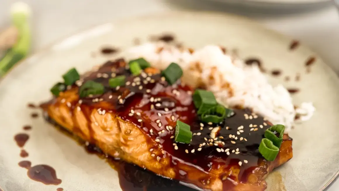 En saftig asiatisk lax med glansig teriyakisås, toppad med sesamfrön och salladslök, serveras med ris.