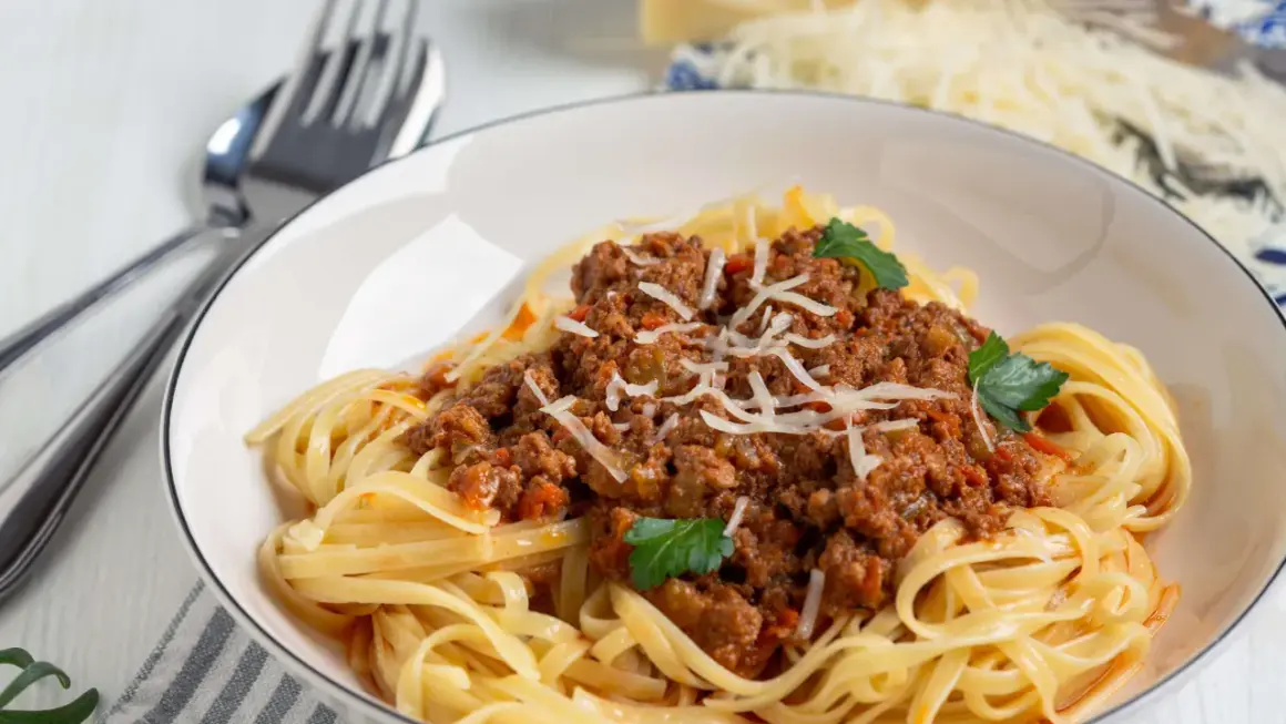 Teller mit Spaghetti Bolognese, garniert mit Parmesan und Petersilie. Ja, man kann gekochte Spaghetti Bolognese einfrieren.