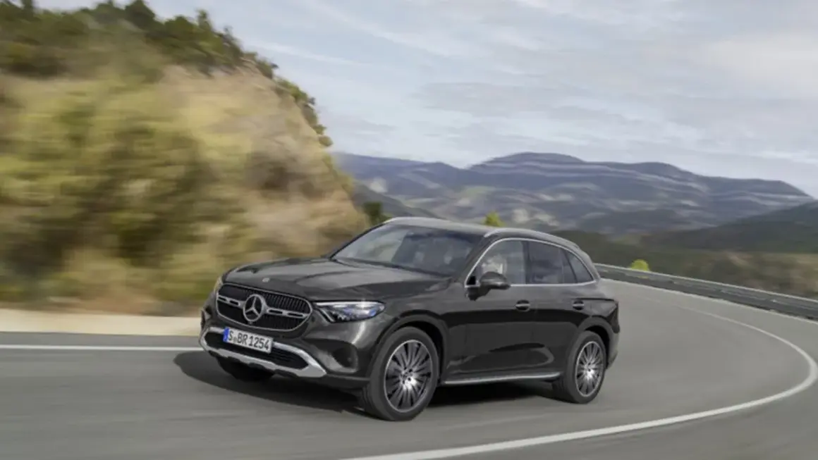Czarny Mercedes GLC 200 4MATIC pokonuje zakręt na górskiej drodze, otoczony zielonymi wzgórzami i skalistymi zboczami.
