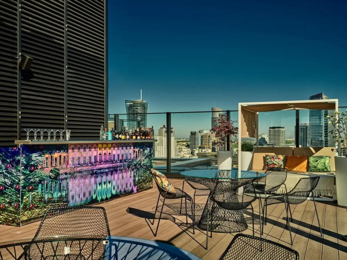 Elegancki ether rooftop bar z widokiem na miasto. Kolorowy bar, stoliki i wygodne fotele zapraszają do relaksu.