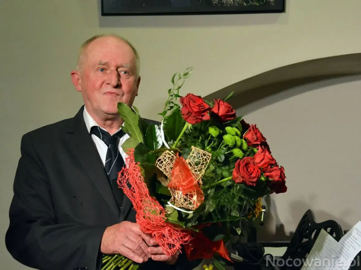 Starszy mężczyzna w garniturze trzyma bukiet czerwonych róż i zielonych kwiatów.