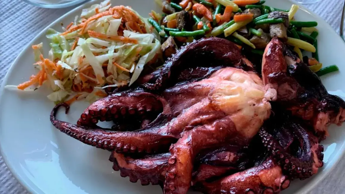 Pulpo entero asado, acompañado de ensalada de col y zanahoria, y verduras salteadas. Un festín digno de los cazadores.