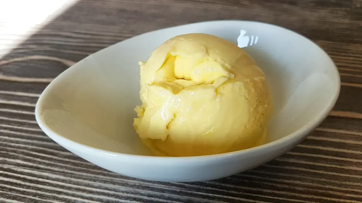 Cremiges Mango-Eis, selbst gemacht mit der Eismaschine, in einer weißen Schale auf Holztisch.