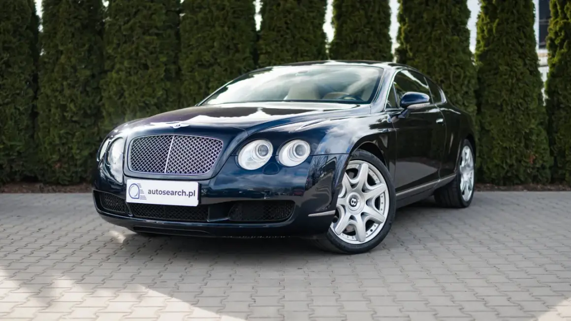 Elegancki, ciemnogranatowy Bentley Continental GT, brytyjski producent luksusowych aut, zaparkowany przed żywopłotem.