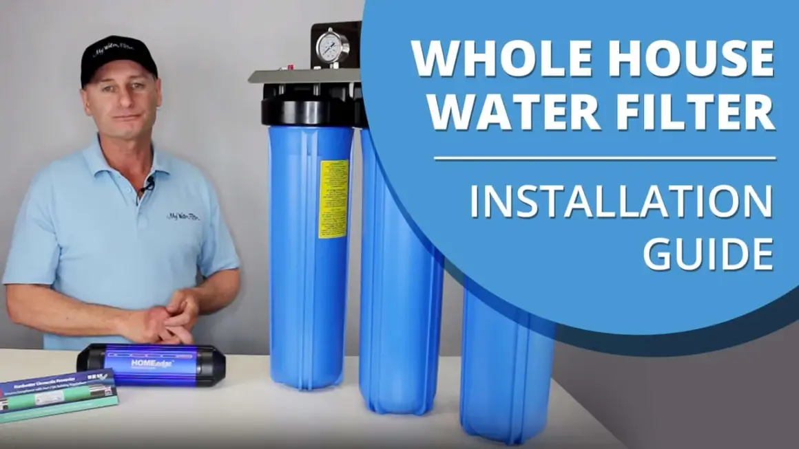 Man in a cap and polo shirt stands next to a whole house water filter system, ready for installation.
