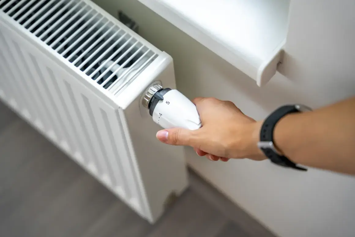 Dłoń reguluje termostat grzejnika. Zastanawiasz się, dlaczego grzejnik jest zimny na dole? Może to być problem z odpowietrzeniem lub cyrkulacją wody.