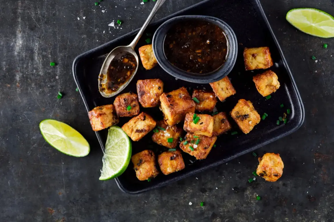Tofu in padella dorato e croccante, servito con salsa e spicchi di lime.