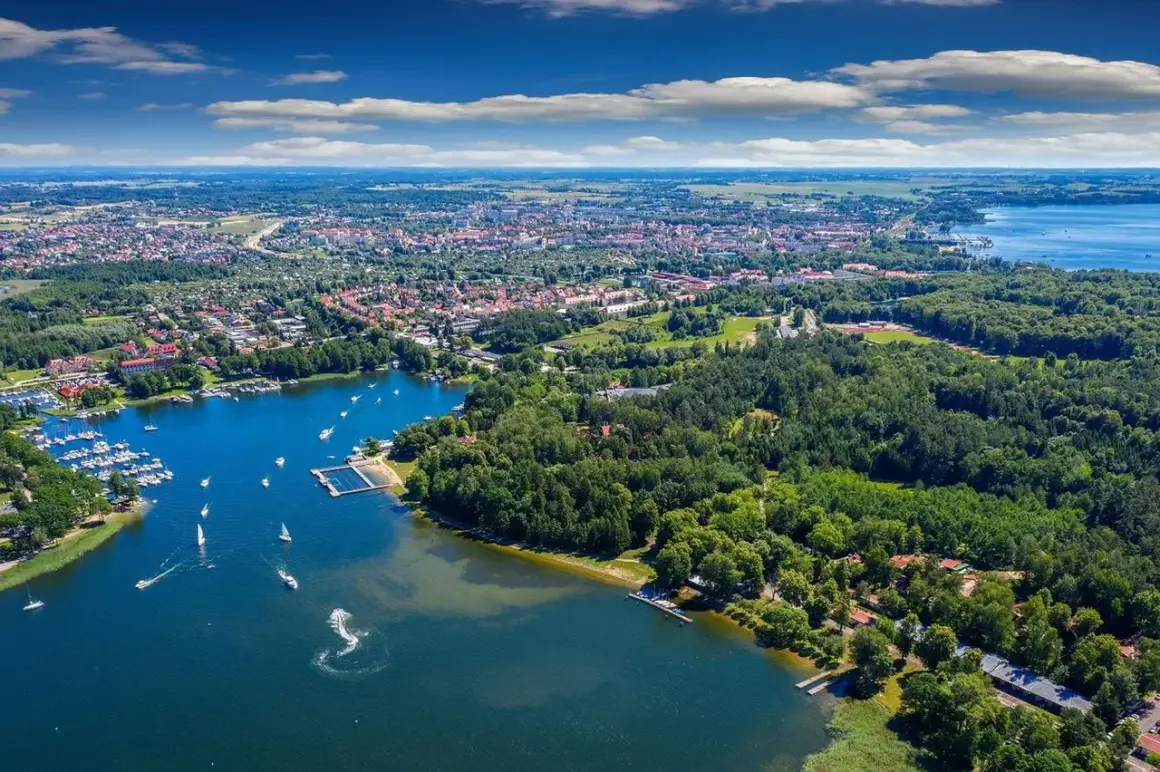 Malownicze jezioro, nad którym leży Giżycko, tętni życiem. Widać tu port jachtowy, plażę i liczne łodzie.