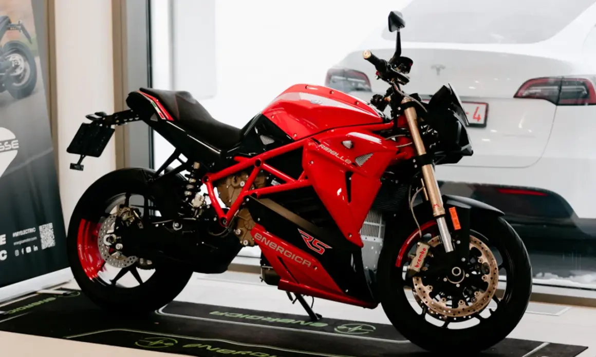 Motocicleta roja y negra Energica RS, lista para la acción. Detrás, un coche blanco.