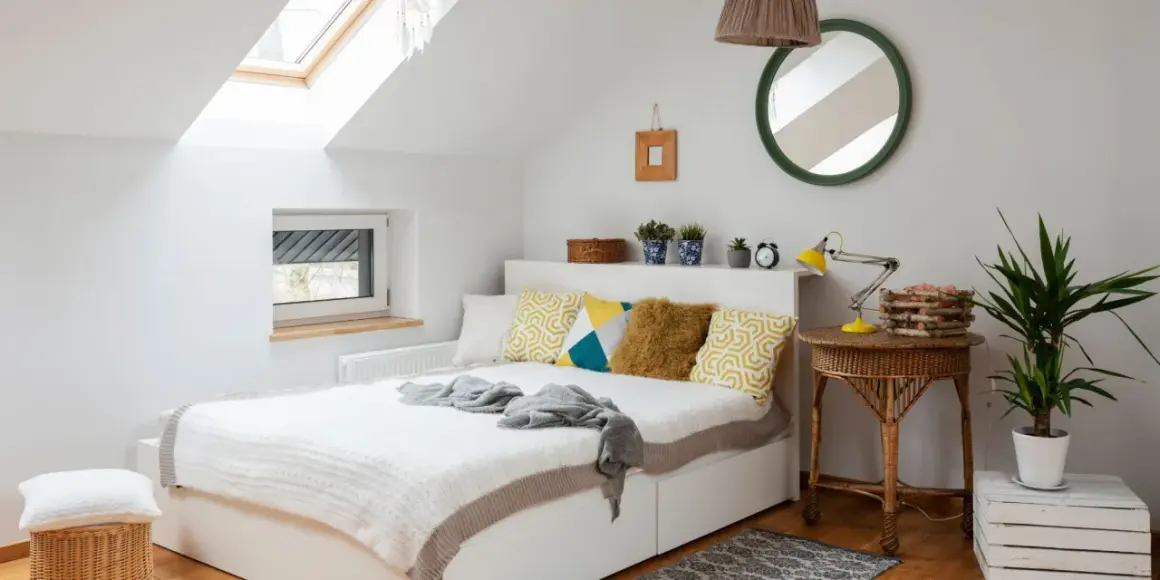 Chambre sous pente lumineuse avec lit blanc, coussins géométriques, et un puits de lumière. Une belle idée peinture pour un espace cosy.
