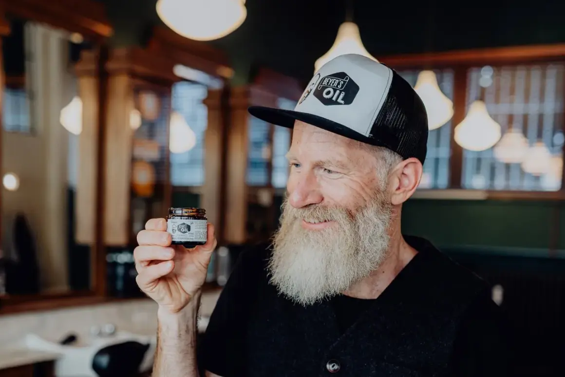 Mann mit Bart hält Tiegel "Beyer's Oil". Perfekt für Bartpflege selber machen.