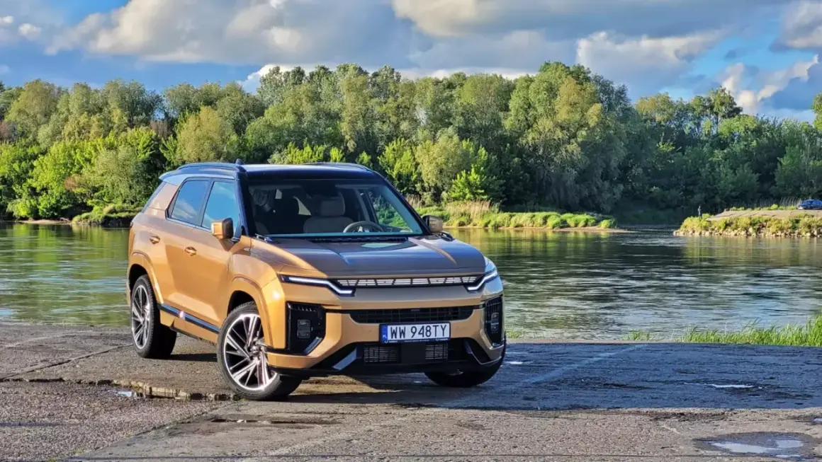Złoty KGM Actyon SUV stoi nad rzeką, otoczony zielenią.
