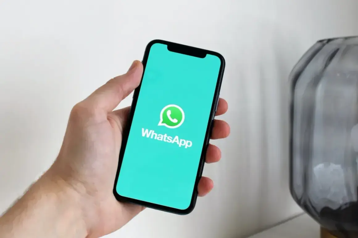 Dłoń trzyma smartfon z logo WhatsApp. Aplikacja istnieje od 2009 roku, co oznacza, że ma już ponad dekadę!