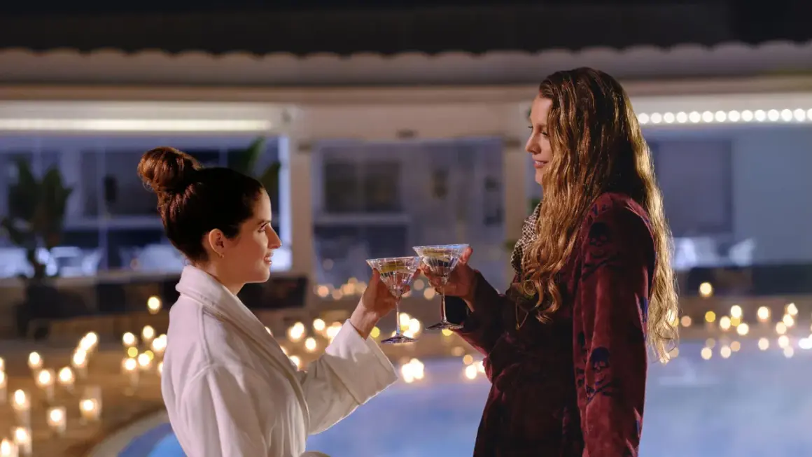 Zwei Frauen stoßen mit Martinis an, umgeben von Kerzenlicht und einem Pool. Nur noch ein kleiner gefallen, bevor der Abend perfekt ist.