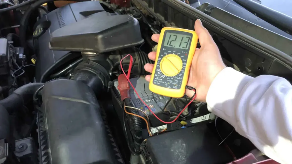 Multimetr pokazuje 12.13V, co jest kluczowe, by sprawdzić czy bateria jest naładowana. Pomiar napięcia akumulatora samochodowego.