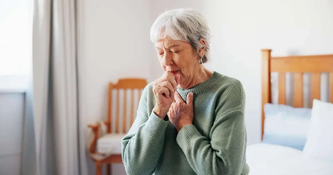 Ältere Frau hustet, kämpft mit Atemnot. Asthma kann zu einer Schwerbehinderung führen und den Alltag stark beeinträchtigen.