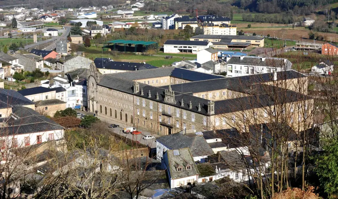 Vista aérea del monasterio de Mondoñedo, un imponente edificio de piedra con tejados oscuros, rodeado de casas y vegetación.
