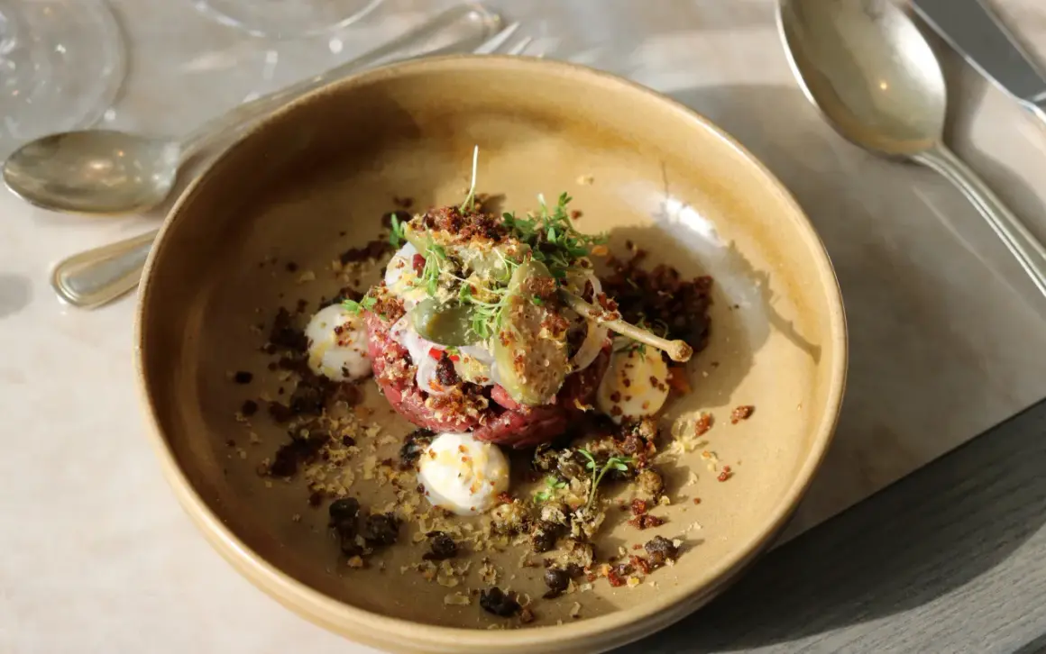 En konstnärlig råbiff med kapris, ägg och örter, serverad i en rustik skål. En kulinarisk upplevelse från Fjelie vingård.