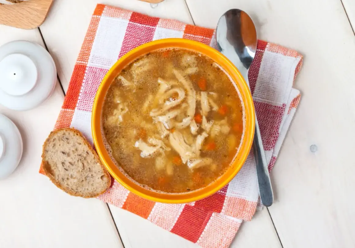 Pyszne flaki Ani gotuje, podane w pomarańczowej misce z chlebem i łyżką.