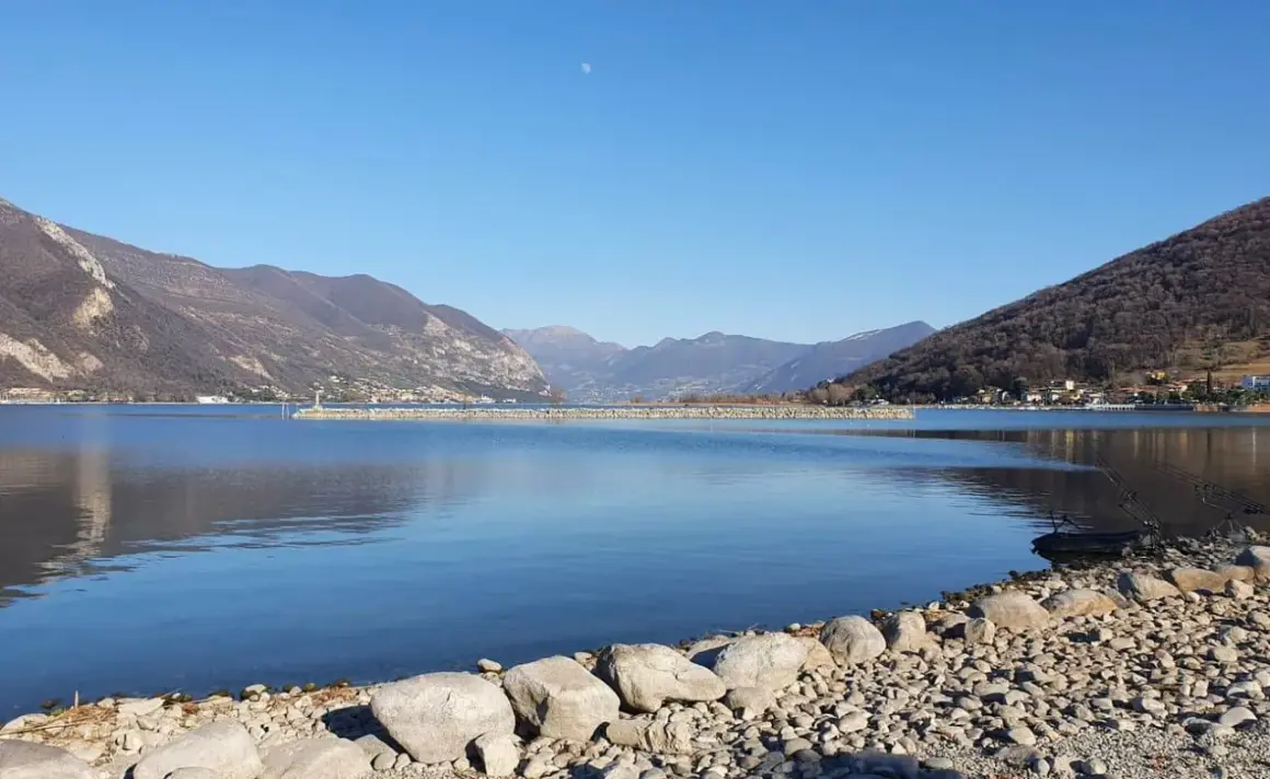 Calm lake with mountains in the background and a rocky shore in the foreground.