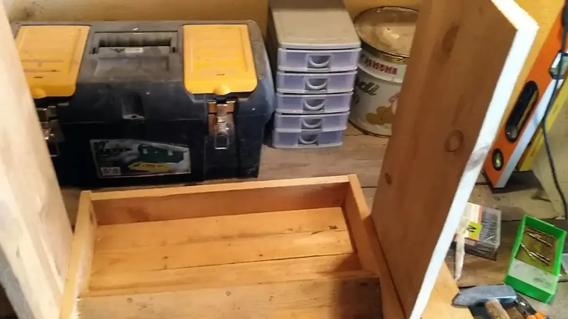 Costruzione di una mangiatoia per galline fai da te. In primo piano, una struttura in legno grezzo. Sullo sfondo, una cassetta degli attrezzi, contenitori a cassetti e una livella.