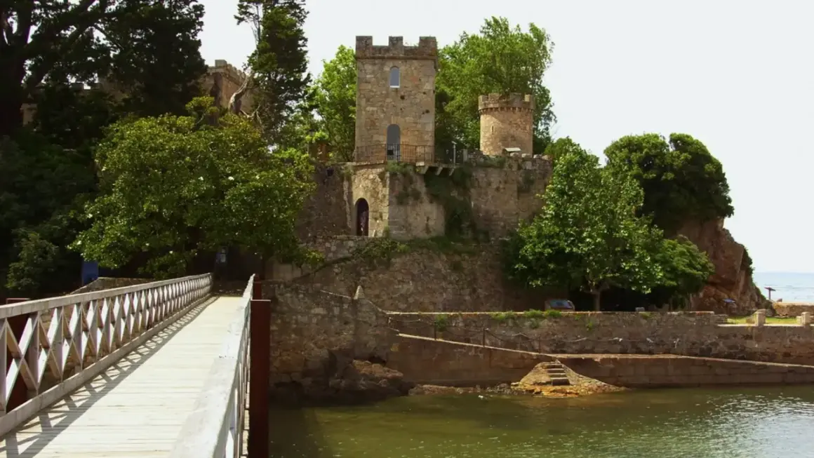 Un puente de madera conduce al histórico castillo de Santa Cruz, rodeado de exuberante vegetación y con vistas al mar.