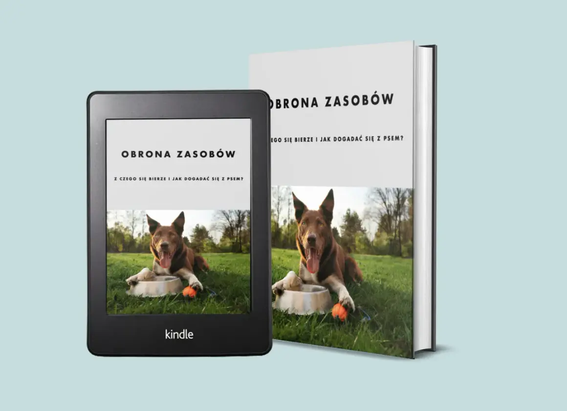 Książka i czytnik Kindle o obronie zasobów u psa. Pies leży na trawie przy misce z zabawką.