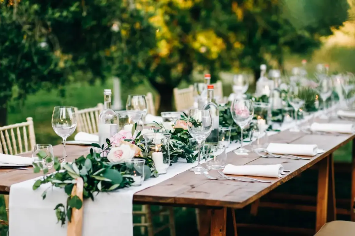 Tavola apparecchiata all'aperto con candele, fiori e bicchieri. Un esempio di addobbi tavoli matrimonio fai da te, con un tocco rustico ed elegante.