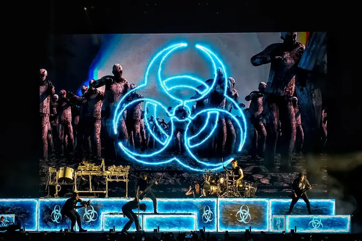 Koncertowy zespół na tle ekranu z symbolem biohazard i zombie.