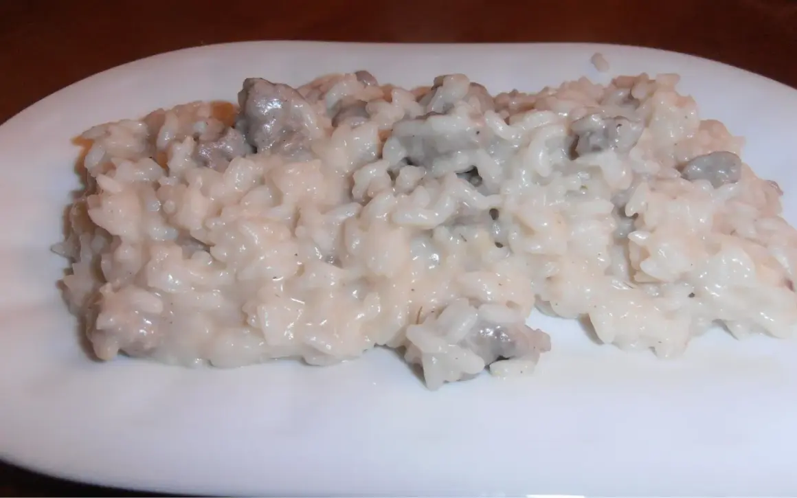 Un cremoso risotto salsiccia e patate, servito su un piatto bianco.