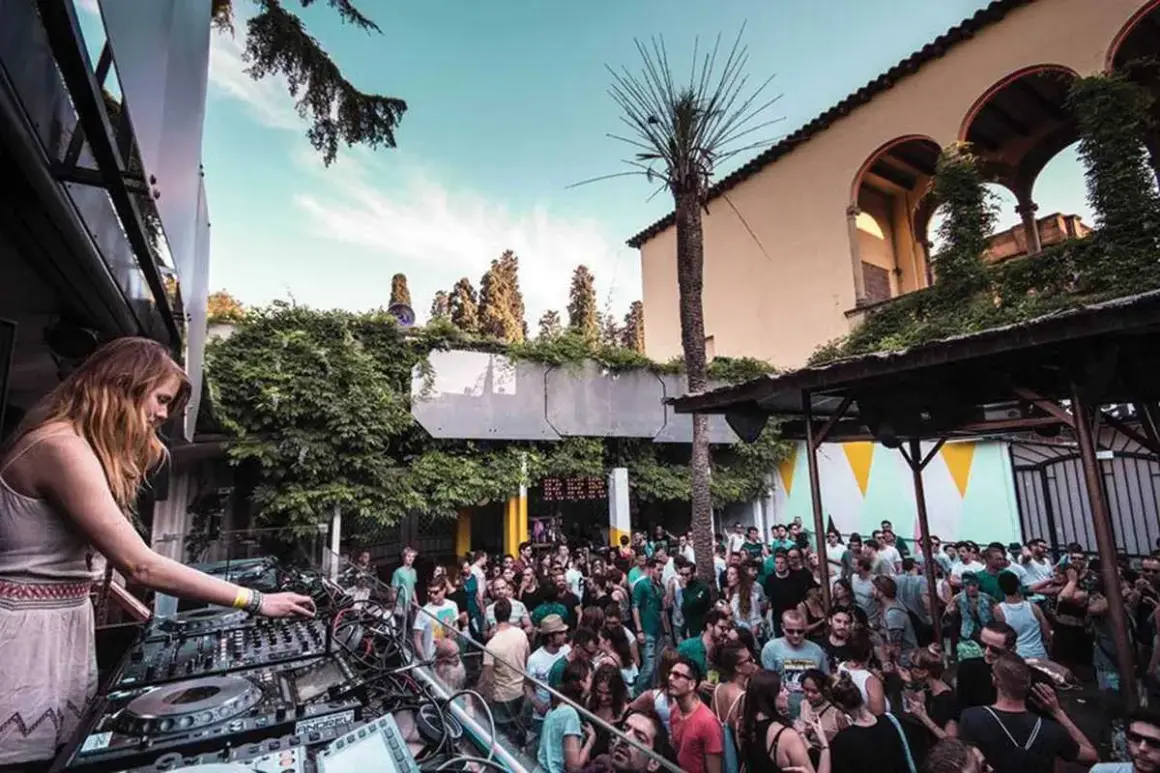 DJ set su una terrazza a Barcellona, con folla che balla sotto il cielo azzurro.