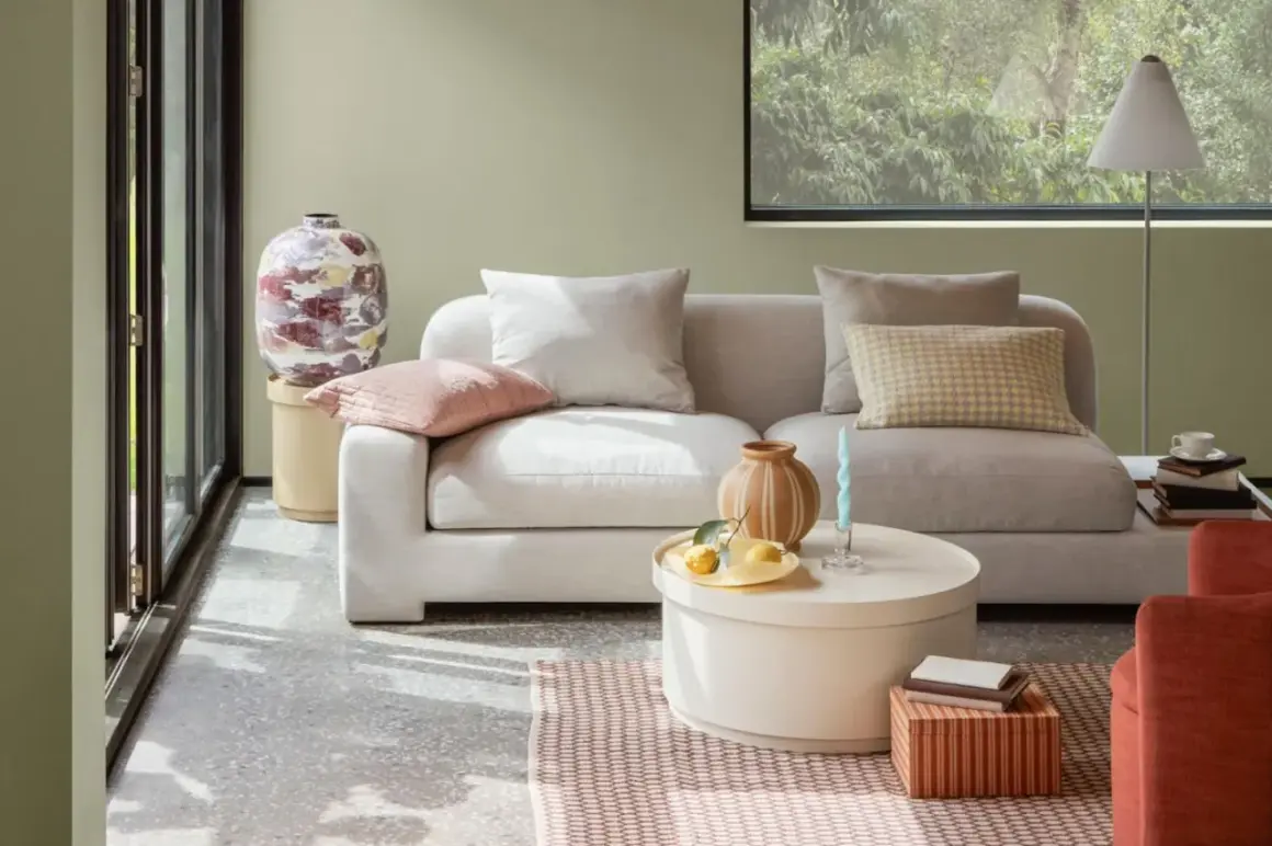 Gemütliches Wohnzimmer mit hellgrauem Sofa, Kissen in sanften sommer farben und einem runden Couchtisch.