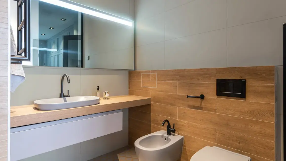 Bagno moderno con lavabo ovale, bidet e WC. Le pareti sono rivestite con piastrelle effetto legno e grigie, un mix che offre ottime opinioni per chi ama il design.