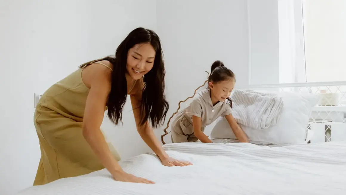 Mutter und Kind machen das Bett frisch. Der Boxspringbett Topper wellt sich leicht, während sie die Bettwäsche glattziehen.