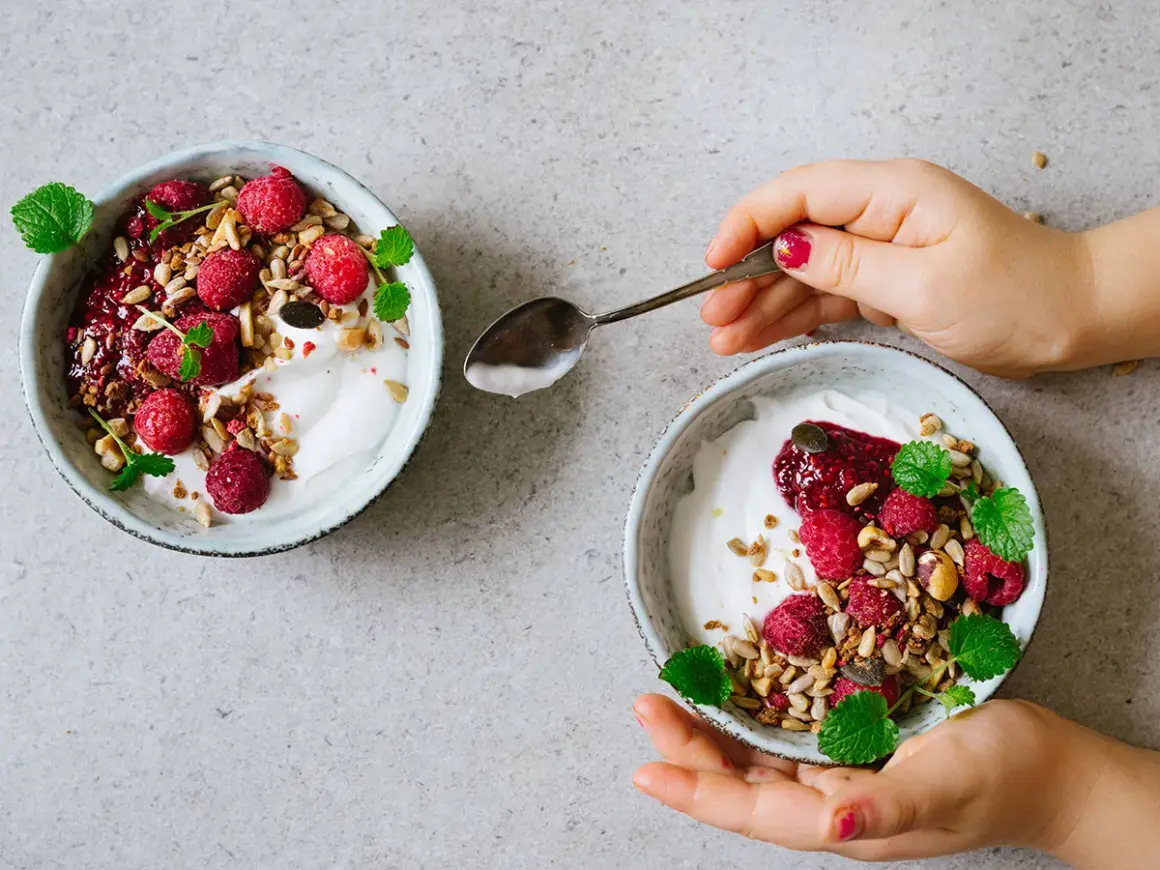 Två skålar med kokosyoghurt, hallon, granola och mynta. Perfekt för ett enkelt kokosyoghurt recept.