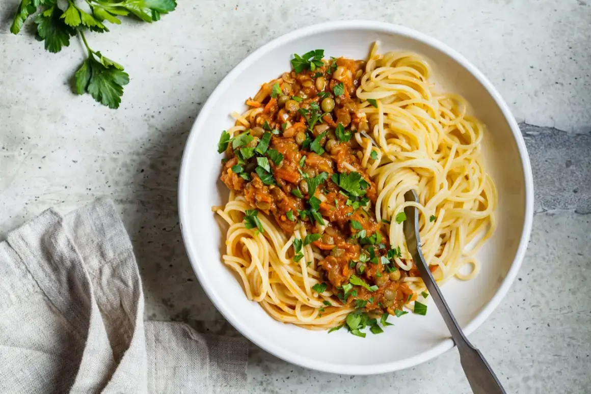 Porcja spaghetti z sosem z soczewicy i warzyw, posypana natką pietruszki. Zdjęcie sugeruje zdrowe spaghetti kcal.