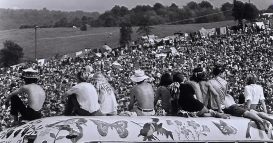 Widok z góry na tłum ludzi na festiwalu Woodstock '69, z kilkoma osobami siedzącymi na ozdobionej ciężarówce.