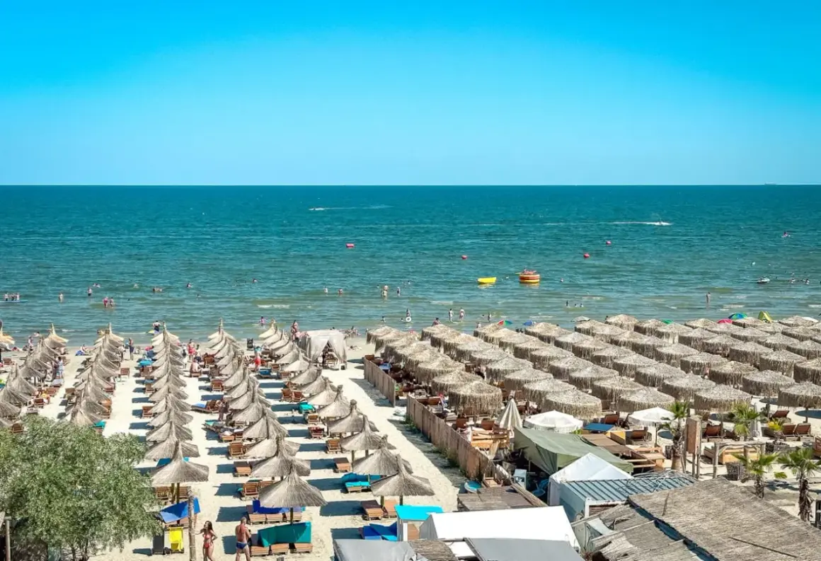 Słoneczne rumuńskie wakacje nad Morzem Czarnym. Plaża pełna leżaków i parasoli, ludzie kąpią się i relaksują.