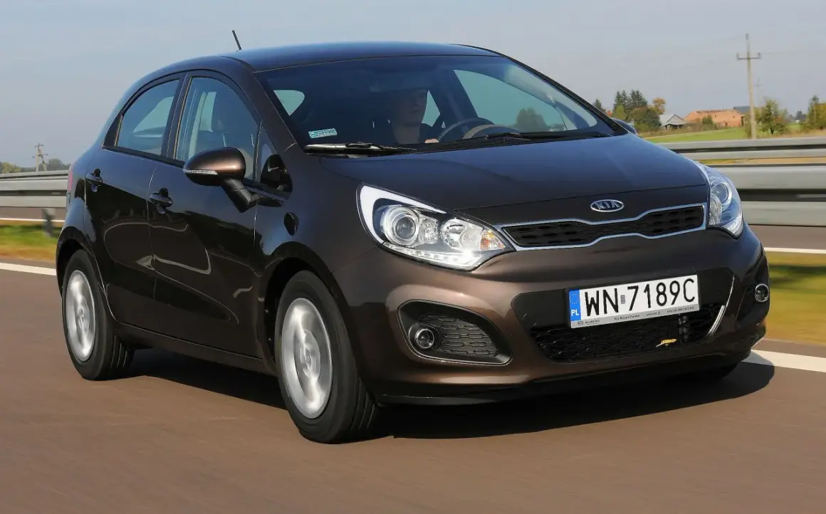 Brązowe Kia Rio 3 w ruchu drogowym, z widocznym kierowcą i tablicą rejestracyjną WN-7189C.