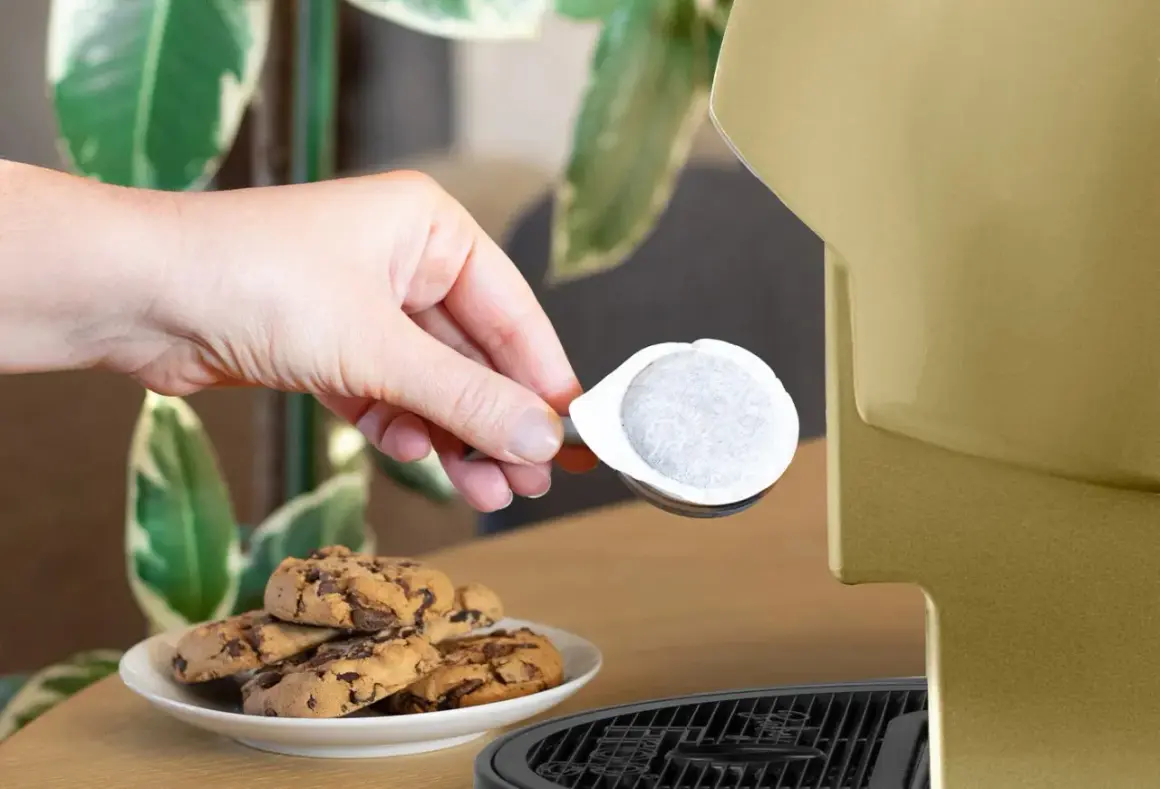 Una mano inserisce una cialda ese, perfetta per un caffè veloce, accanto a biscotti al cioccolato.