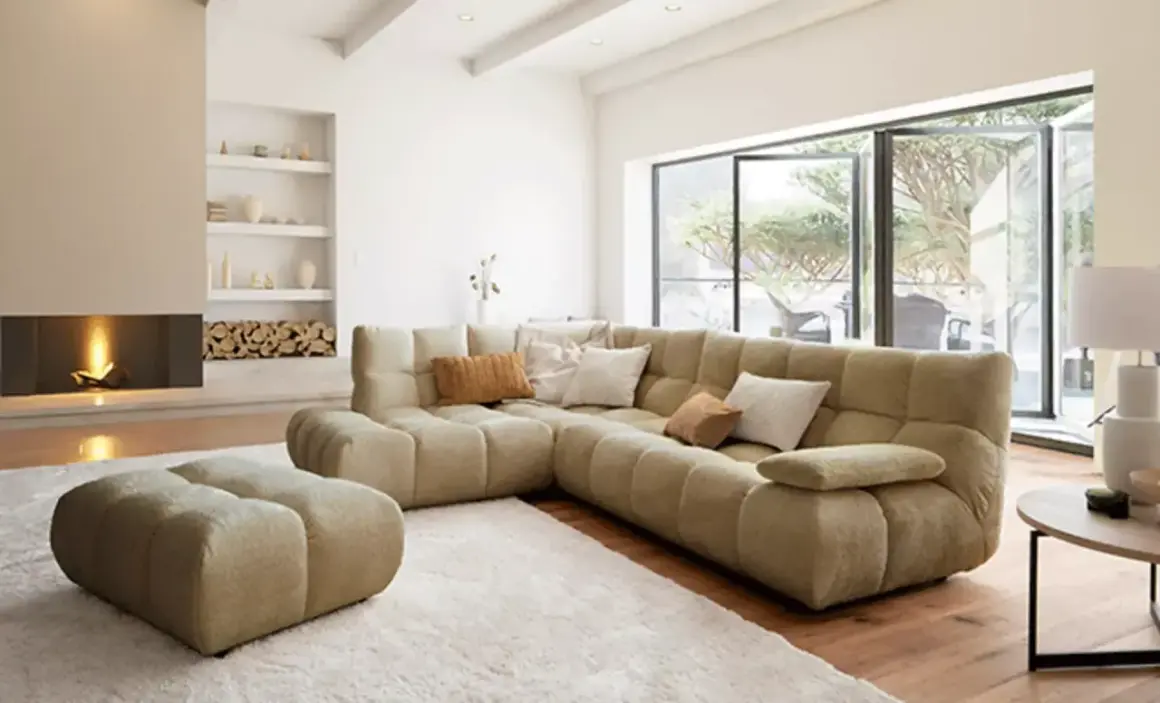 Gemütliches Wohnzimmer mit großem Ecksofa, Kamin und Blick in den Garten – ein Ausblick auf die wohntrends 2026.