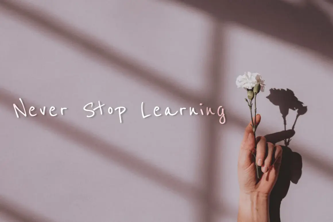 Dłoń trzyma biały kwiat. Napis "Never Stop Learning" przypomina o mądrych cytatach o szkole i ciągłym rozwoju.