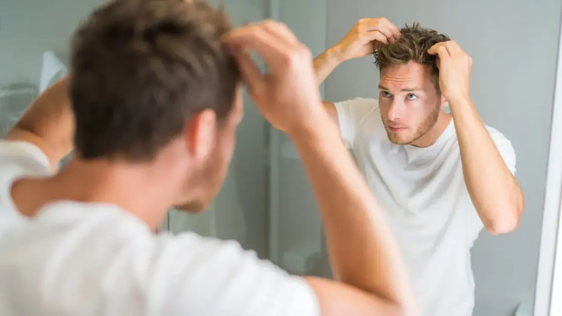 Ein Mann mit strohigem Haar stylt sich vor dem Spiegel.