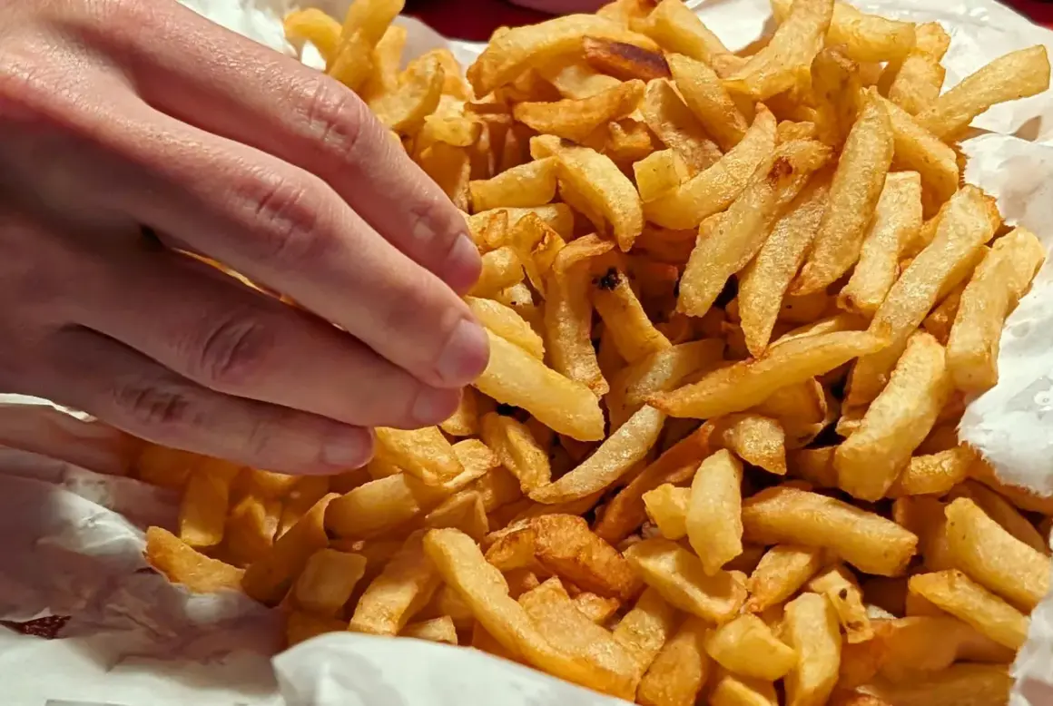 En hand plockar en gyllene pommes frites ur en stor hög med krispiga pommes frites.