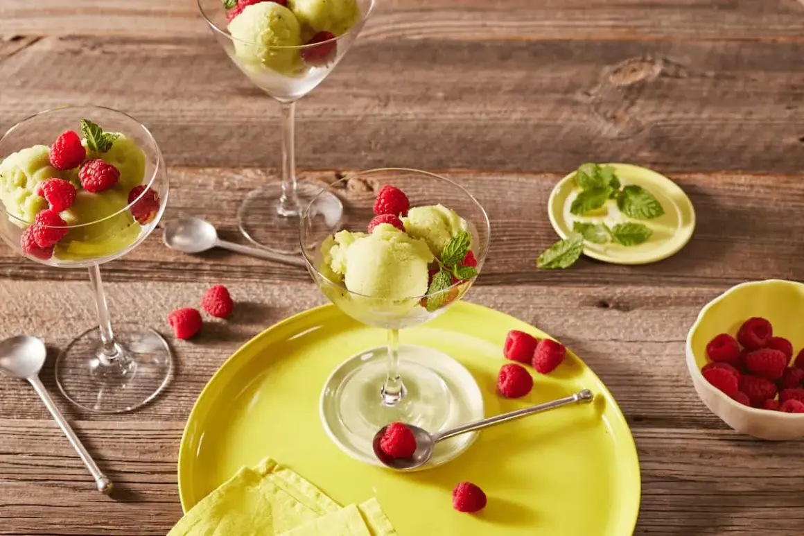 Erfrischendes Kiwi-Sorbet mit Himbeeren und Minze in eleganten Gläsern auf Holzhintergrund.