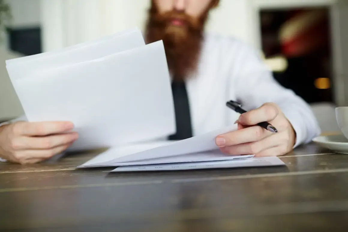 Hombre con barba revisa documentos, evaluando la validez del contrato de alquiler sin registrar.