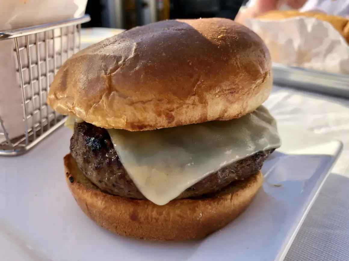 Hamburger z serem na białym talerzu, obok koszyka na frytki.
