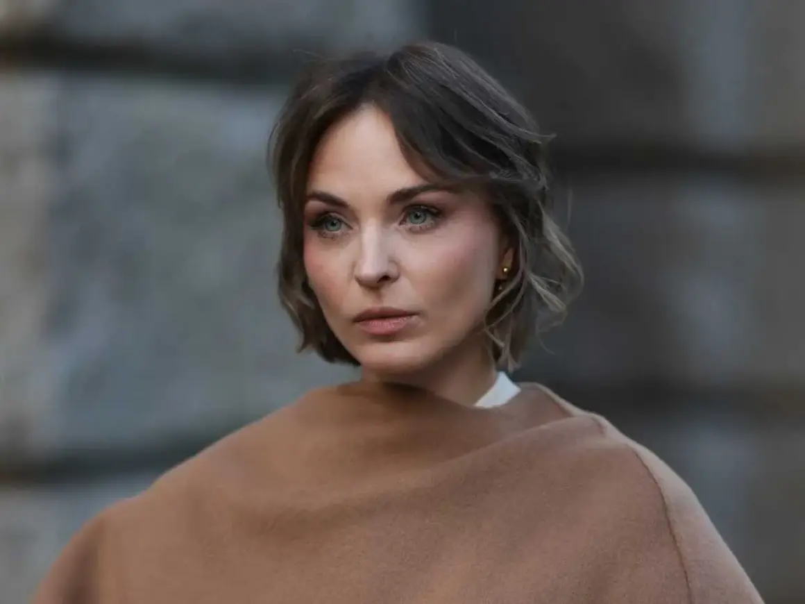 Eine Frau mit Kurzhaarfrisuren und einem leicht molligen Gesicht blickt nachdenklich in die Ferne, eingehüllt in einen braunen Schal.