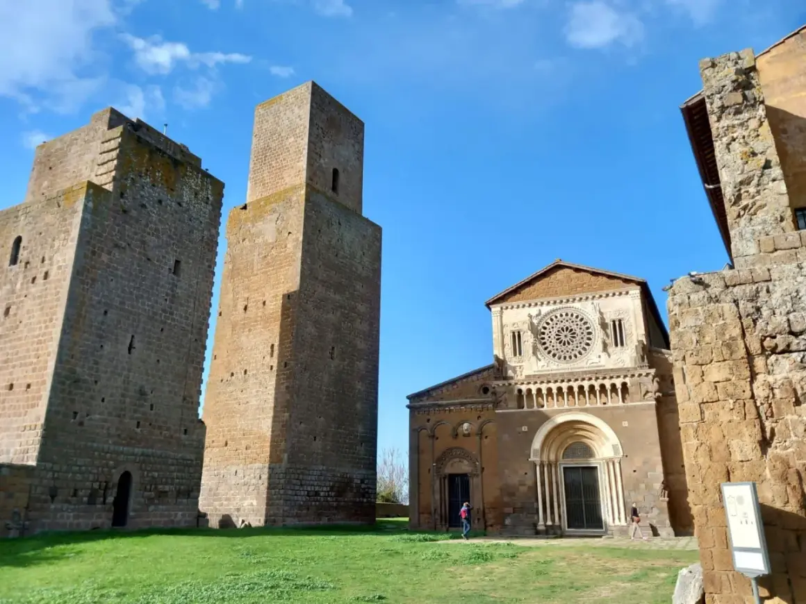 Le chiese di Tuscania, con le loro torri medievali e la facciata romanica, si stagliano contro un cielo azzurro.