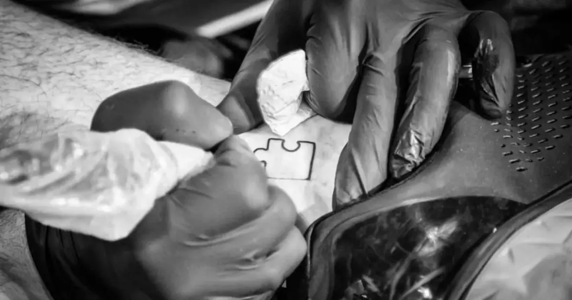 Ręce w rękawiczkach tworzą tatuaż puzzle, symbol autyzmu.